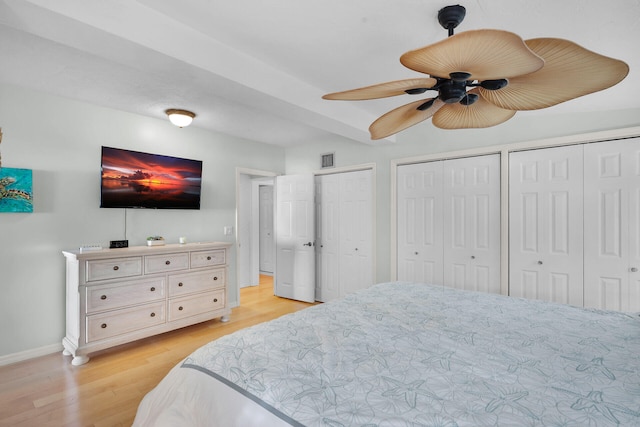 bedroom with baseboards, light wood-style floors, visible vents, and two closets