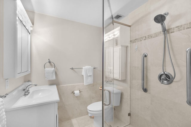 bathroom featuring a stall shower, tile walls, toilet, visible vents, and vanity