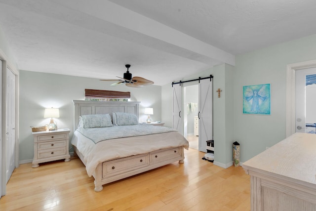 bedroom with a barn door, light wood-type flooring, and baseboards