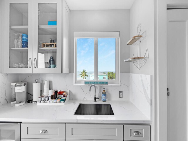 bar featuring light stone counters, sink, backsplash, and white cabinets