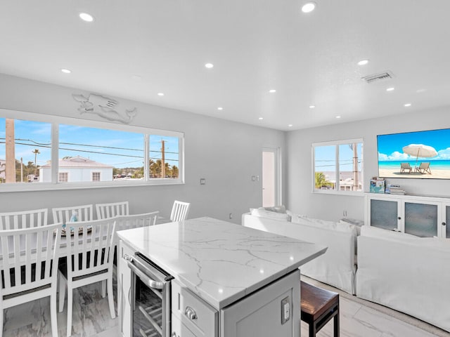 kitchen with a breakfast bar, beverage cooler, light stone countertops, and a wealth of natural light