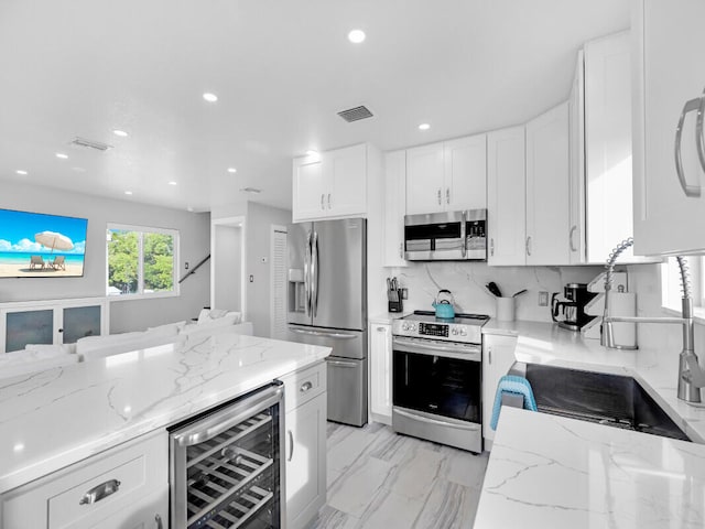 kitchen featuring light stone counters, tasteful backsplash, stainless steel appliances, beverage cooler, and white cabinets