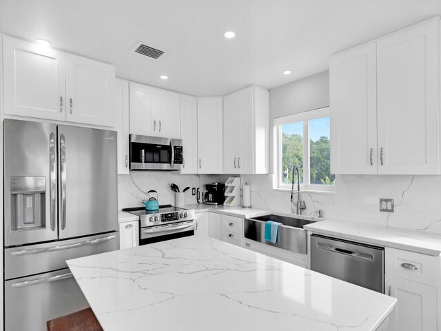 kitchen with sink, white cabinetry, tasteful backsplash, appliances with stainless steel finishes, and light stone countertops