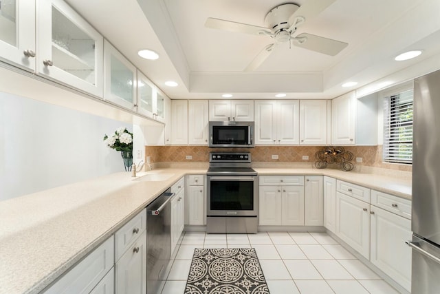 kitchen featuring a tray ceiling, a sink, decorative backsplash, light countertops, and stainless steel appliances