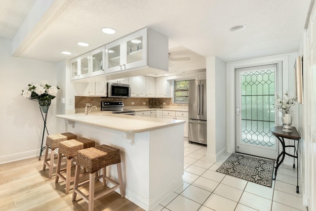 kitchen with glass insert cabinets, a breakfast bar area, decorative backsplash, a peninsula, and stainless steel appliances