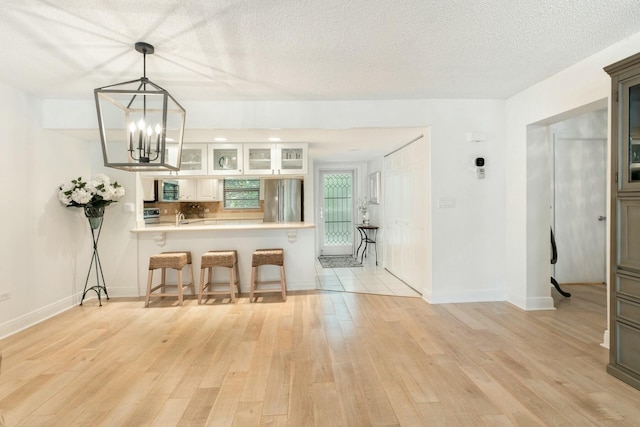 kitchen featuring glass insert cabinets, light wood finished floors, a breakfast bar, and freestanding refrigerator