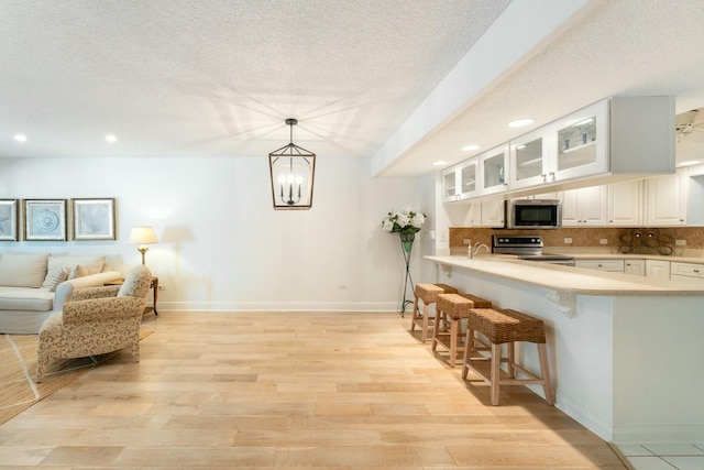 kitchen with a kitchen bar, backsplash, light wood-style floors, appliances with stainless steel finishes, and light countertops