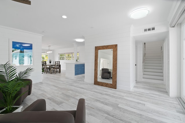 living room with wooden walls, ornamental molding, and light wood-type flooring