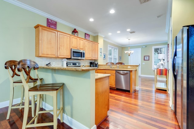 kitchen with appliances with stainless steel finishes, decorative light fixtures, kitchen peninsula, and a breakfast bar area