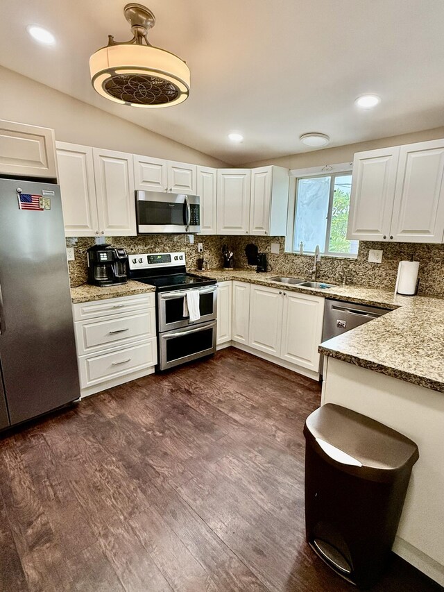 kitchen with vaulted ceiling, appliances with stainless steel finishes, sink, white cabinets, and light stone counters