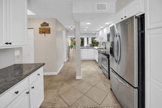 kitchen with appliances with stainless steel finishes, light tile patterned flooring, white cabinets, dark stone counters, and recessed lighting