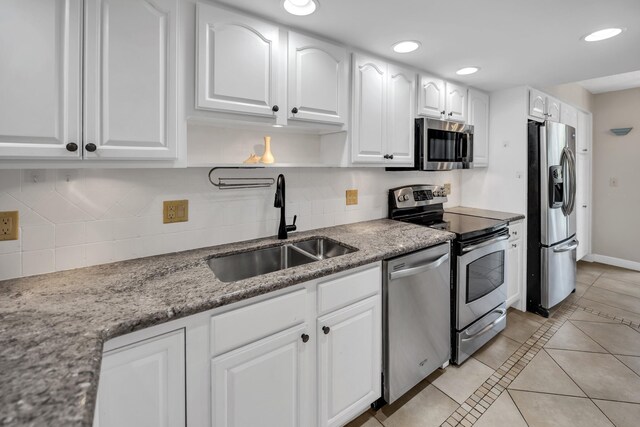 kitchen featuring stainless steel appliances, a sink, light tile patterned floors, white cabinetry, and backsplash