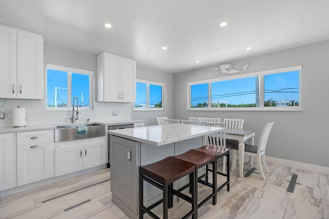 kitchen with a sink, recessed lighting, white cabinets, a kitchen bar, and light stone countertops