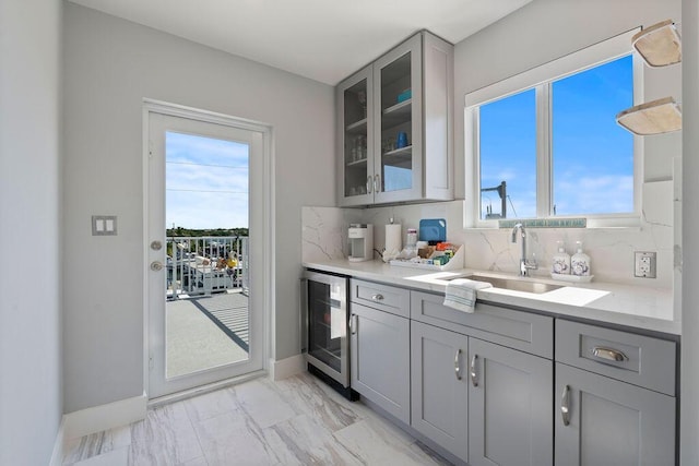bar featuring wine cooler, a sink, tasteful backsplash, light marble finish flooring, and baseboards