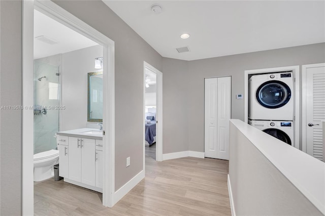 hall featuring stacked washer and clothes dryer, sink, and light wood-type flooring