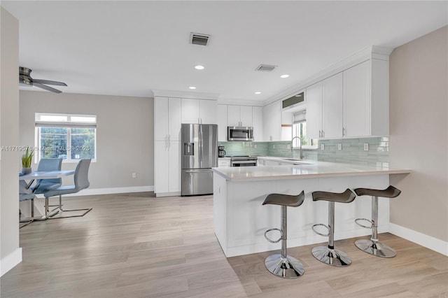 kitchen with appliances with stainless steel finishes, a kitchen breakfast bar, tasteful backsplash, white cabinets, and kitchen peninsula
