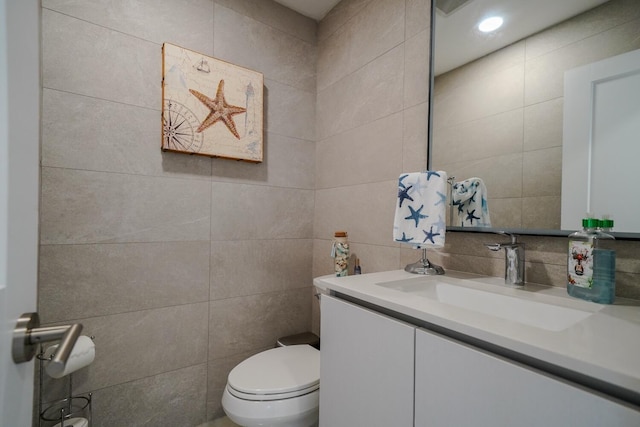 bathroom with vanity, toilet, and tile walls