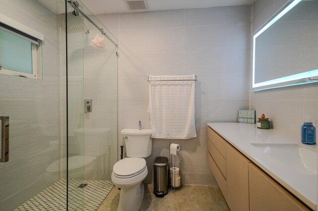 bathroom with tile walls, vanity, toilet, and walk in shower