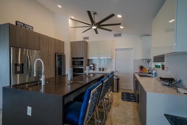 kitchen with sink, a kitchen island with sink, stainless steel appliances, wine cooler, and white cabinets