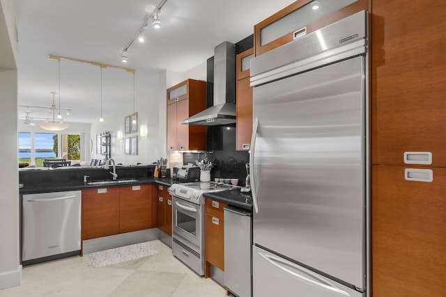 kitchen with pendant lighting, wall chimney range hood, sink, stainless steel appliances, and tasteful backsplash