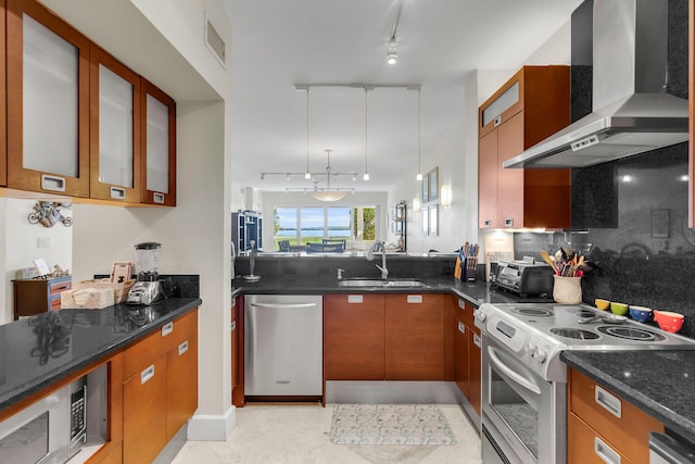 kitchen with wall chimney exhaust hood, sink, hanging light fixtures, dark stone countertops, and stainless steel appliances