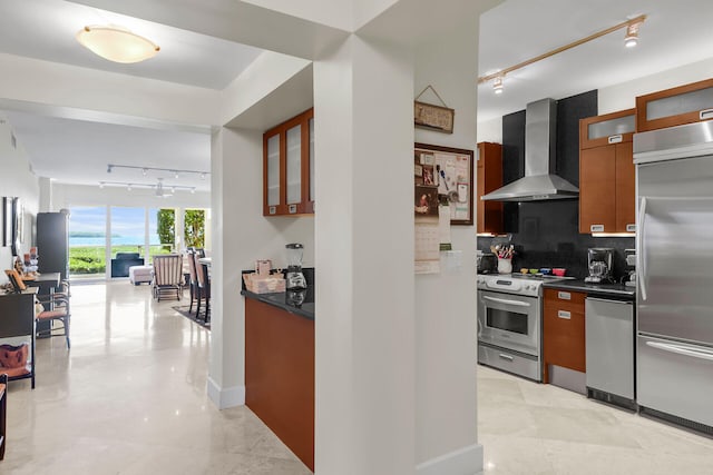 kitchen with tasteful backsplash, rail lighting, wall chimney exhaust hood, and appliances with stainless steel finishes