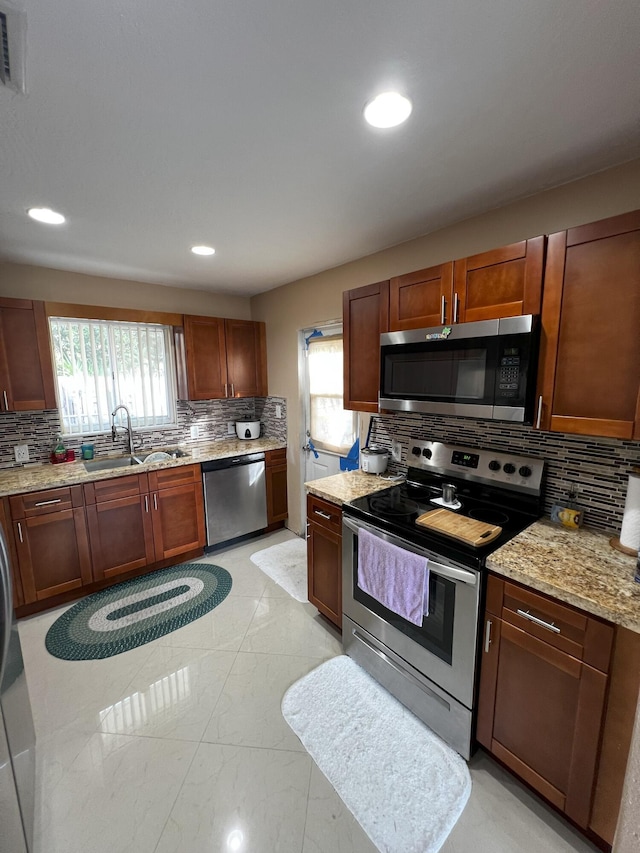 kitchen with appliances with stainless steel finishes, sink, backsplash, and light stone counters