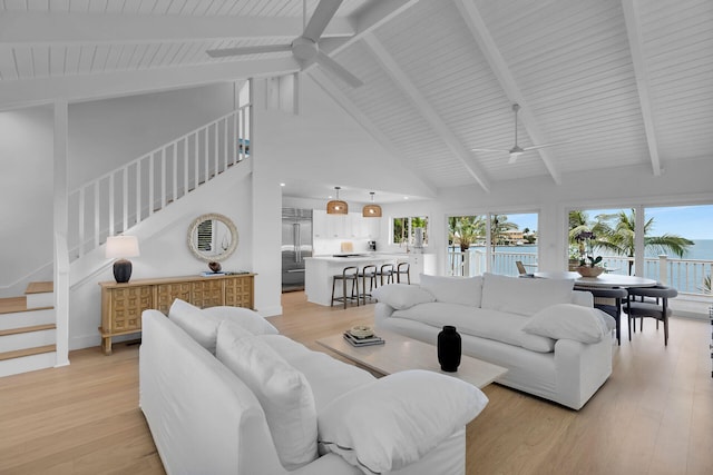 living room featuring beam ceiling, ceiling fan, stairway, and light wood finished floors