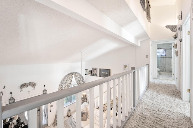 corridor featuring light colored carpet, lofted ceiling with beams, and a textured ceiling