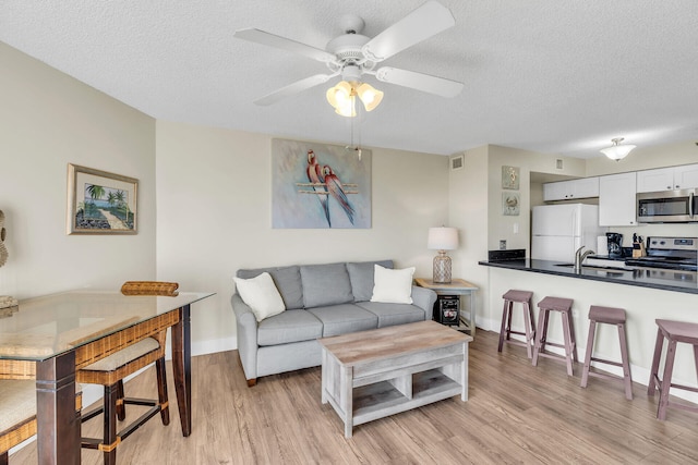 living room featuring sink, light hardwood / wood-style floors, a textured ceiling, and ceiling fan