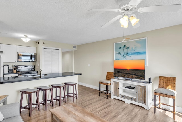 kitchen with white cabinetry, stainless steel appliances, kitchen peninsula, and light hardwood / wood-style flooring