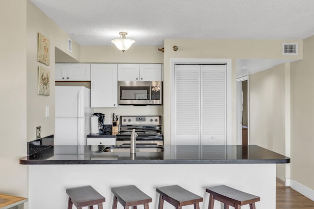 kitchen with white cabinetry, a textured ceiling, a kitchen breakfast bar, kitchen peninsula, and stainless steel appliances