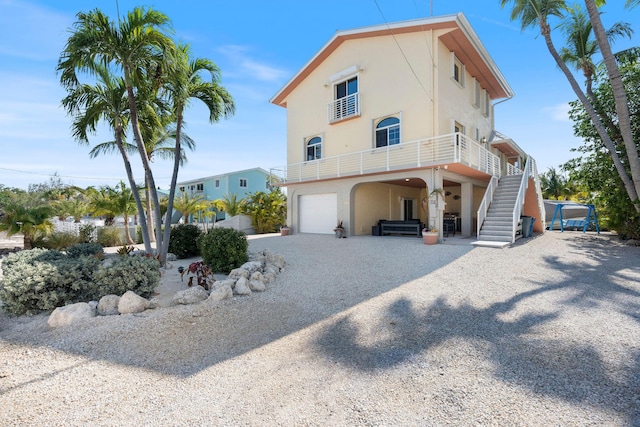 view of property exterior featuring a garage, stucco siding, stairway, a balcony, and gravel driveway