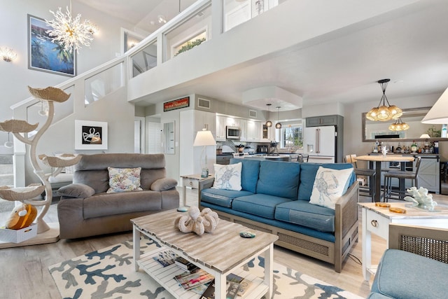 living area featuring a high ceiling, light wood-style flooring, and a notable chandelier