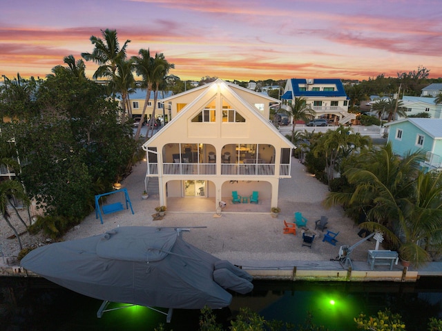 back of property at dusk with stairs, a patio area, a sunroom, and stucco siding