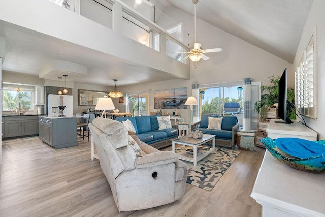 living area with high vaulted ceiling, ceiling fan, and light wood finished floors