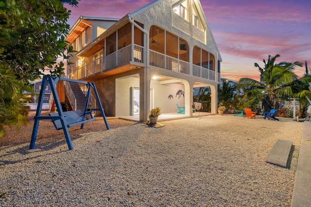 back of house at dusk with a patio, ceiling fan, a sunroom, and stucco siding