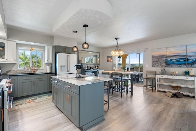 kitchen with stainless steel range, a sink, light wood finished floors, white fridge with ice dispenser, and a kitchen bar