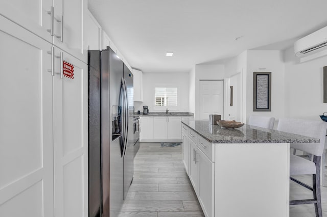 kitchen featuring white cabinetry, dark stone countertops, a breakfast bar area, a center island, and stainless steel fridge with ice dispenser