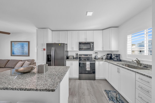 kitchen with sink, white cabinetry, stainless steel appliances, light stone countertops, and light wood-type flooring