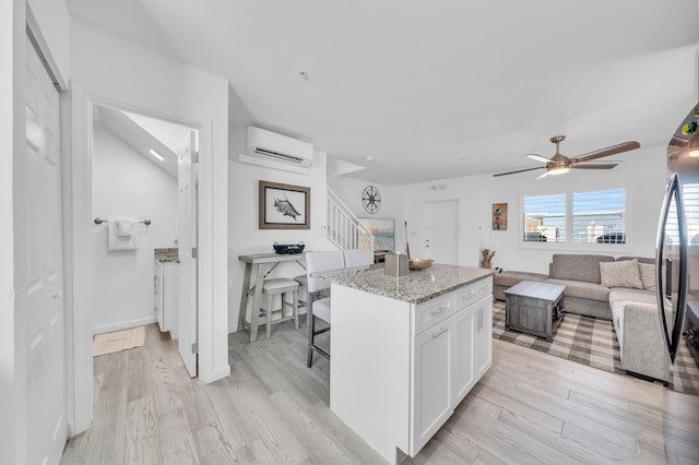 kitchen with a center island, an AC wall unit, a kitchen breakfast bar, light stone countertops, and white cabinets