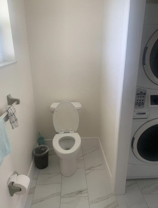 bathroom featuring stacked washer / drying machine and toilet