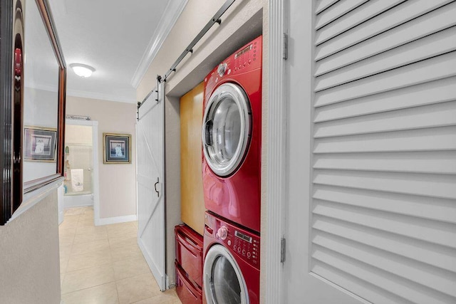 clothes washing area with crown molding, a barn door, stacked washer / dryer, light tile patterned flooring, and laundry area