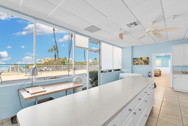 kitchen with light tile patterned flooring, a paneled ceiling, ceiling fan, and white cabinets