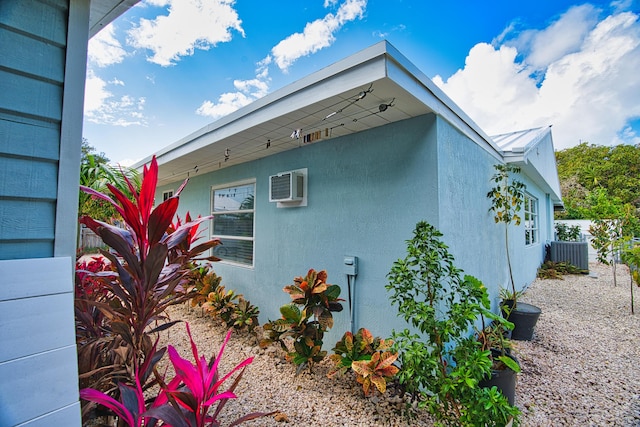 view of side of home featuring fence, a wall mounted air conditioner, stucco siding, cooling unit, and metal roof