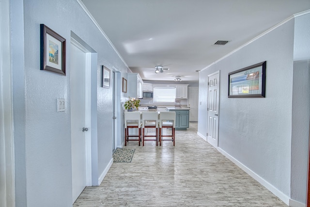 corridor with crown molding, light wood-style flooring, a textured wall, and visible vents