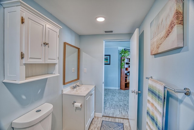 half bath featuring vanity, wood finished floors, visible vents, baseboards, and toilet