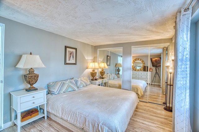 bedroom featuring multiple closets, a textured ceiling, and light wood-style flooring