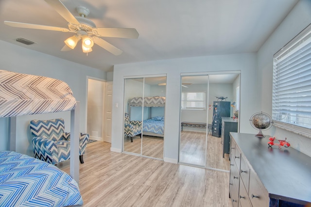 bedroom featuring multiple windows, two closets, light hardwood / wood-style floors, and ceiling fan