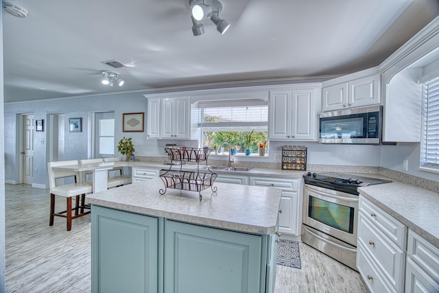 kitchen with a kitchen island, light countertops, white cabinets, stainless steel appliances, and a sink